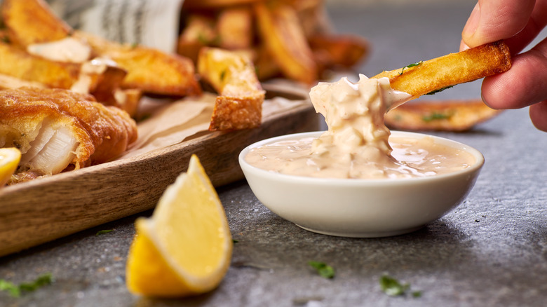 hand dipping fries in sauce