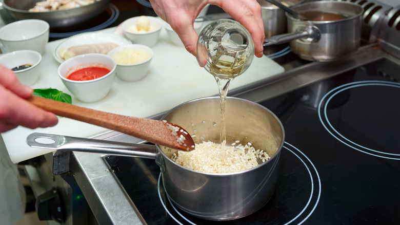 person adding white wine to risotto