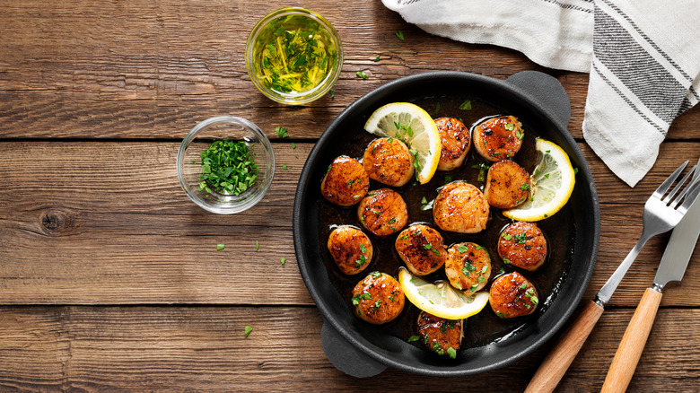 Scallops in pan beside utensils