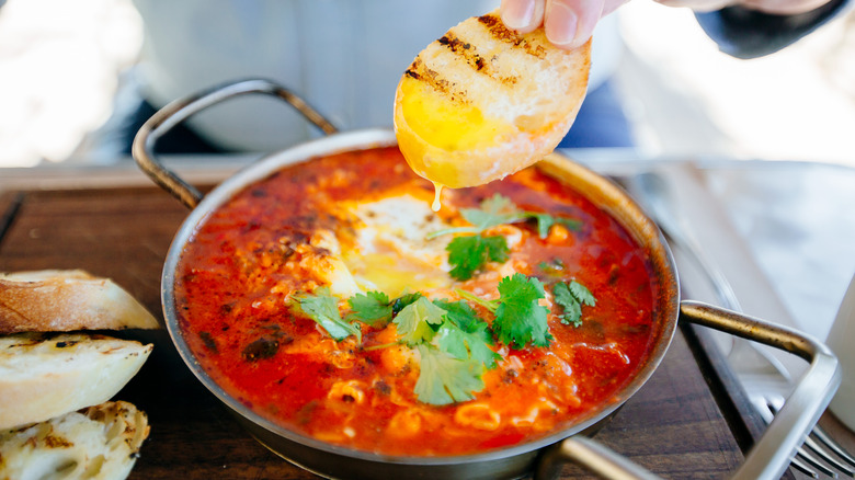 person dipping bread in shakshouka