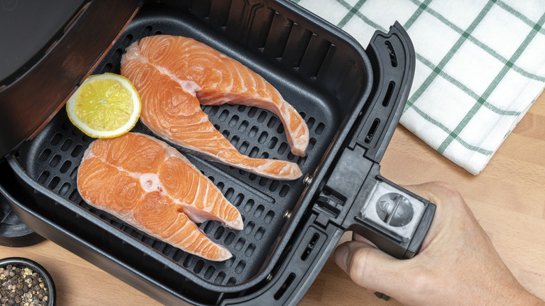 Two salmon steaks with lemon, in an air fryer basket.