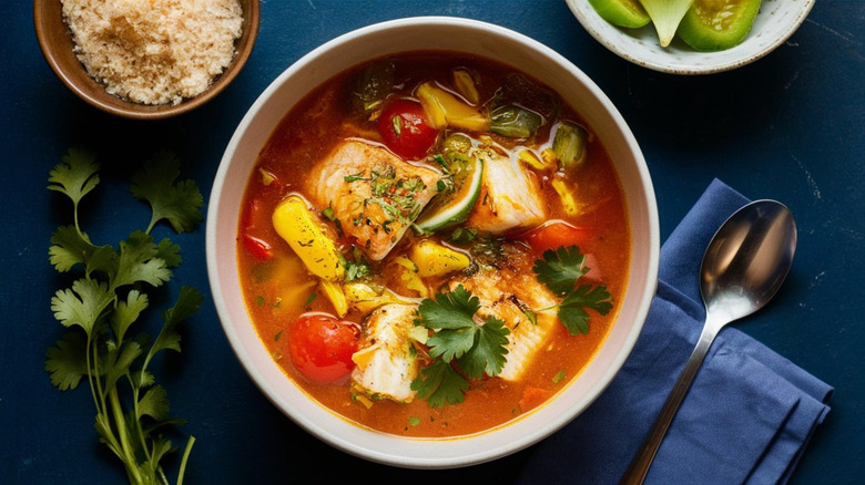 Bowl of fish stew with herbs and vegetables, on a blue tablecloth.