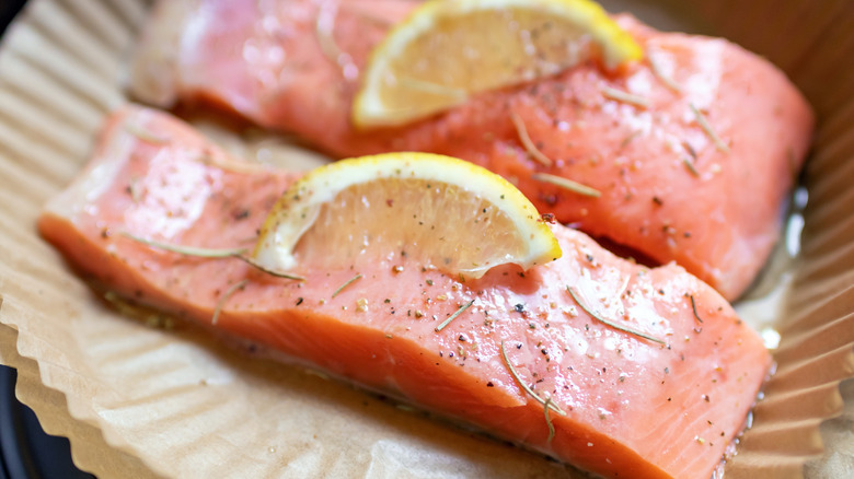 Salmon fillets, with lemon and herbs, on air fryer basket liner.