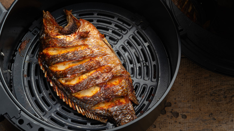 Whole cooked tilapia in air fryer basket.