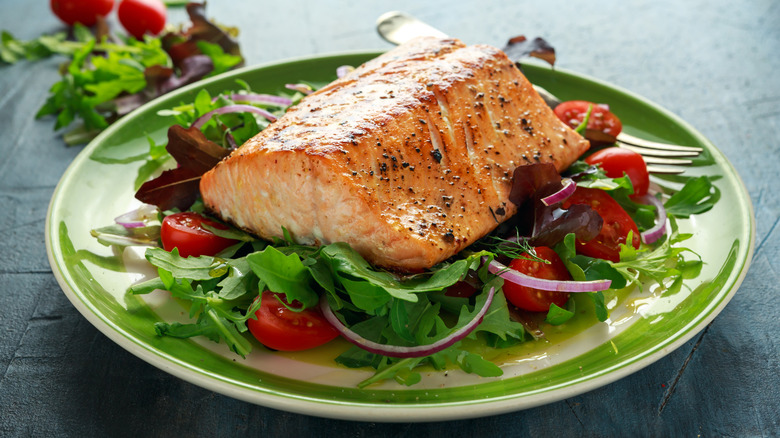 Salmon filet served on top of a salad with arugula, cherry tomatoes, and red onion.