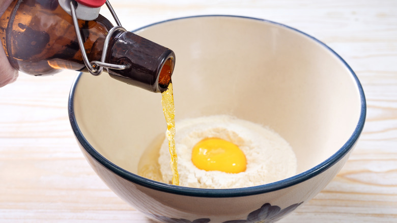 Bottle of beer being poured into batter ingredients.