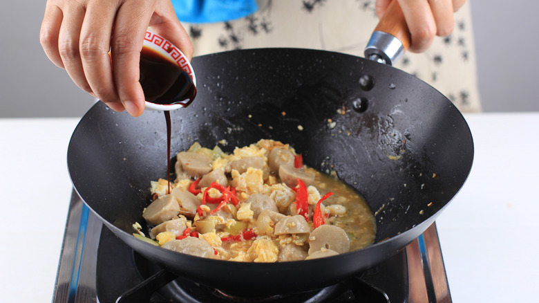 Person adding soy sauce to wok