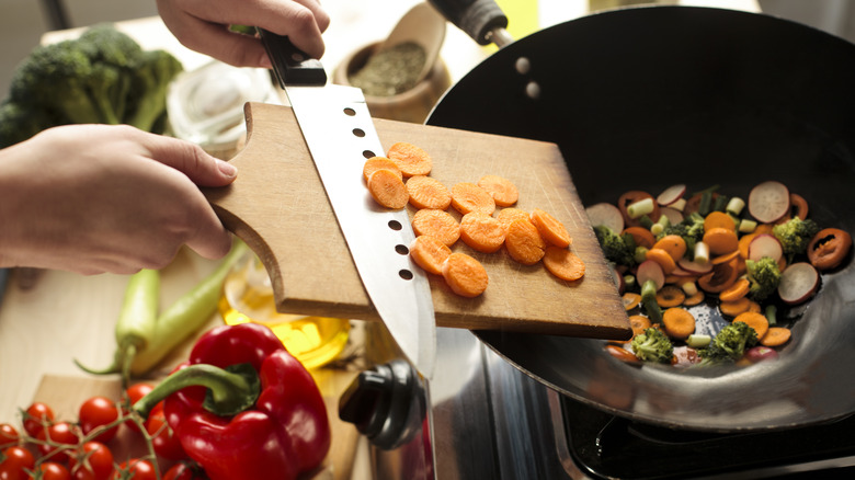 Person putting chopped vegetables in wok