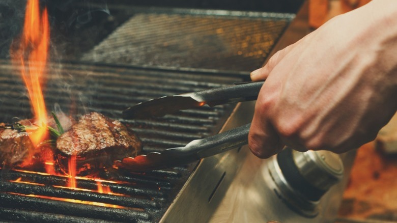 Hand grilling steak with tongs