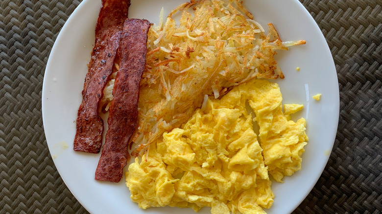 scrambled eggs, bacon and hash browns on white plate