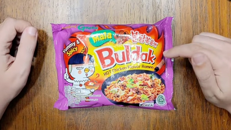 Pack of Buldak Mala Ramen with hands on either side