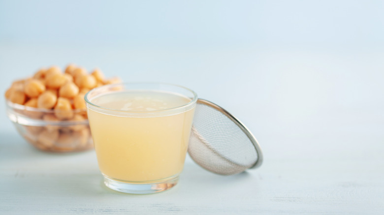 Glass of aquafaba with bowl of chickpeas and small strainer