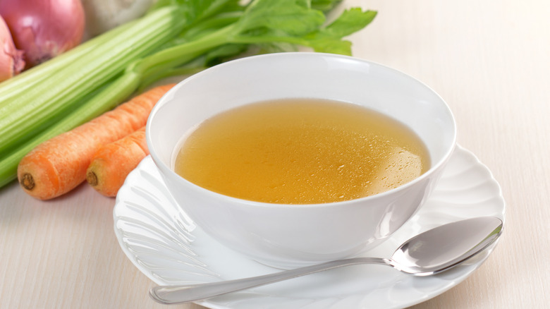 White bowl of chicken broth with fresh vegetables