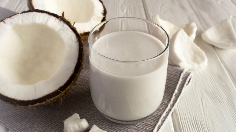 Glass of coconut milk with split coconuts and coconut pieces surrounding it