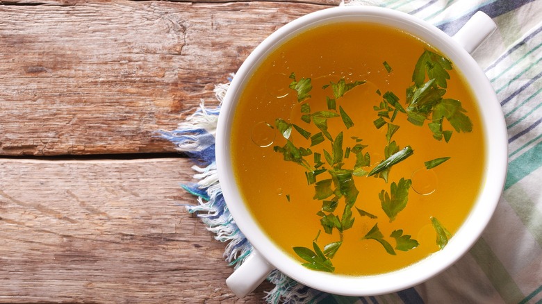 White bowl of chicken broth with parsley