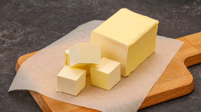 Block of butter and butter cubes sitting on parchment paper on wooden board