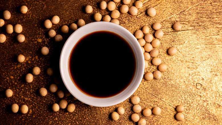 White bowl of soy sauce surrounded by soybeans