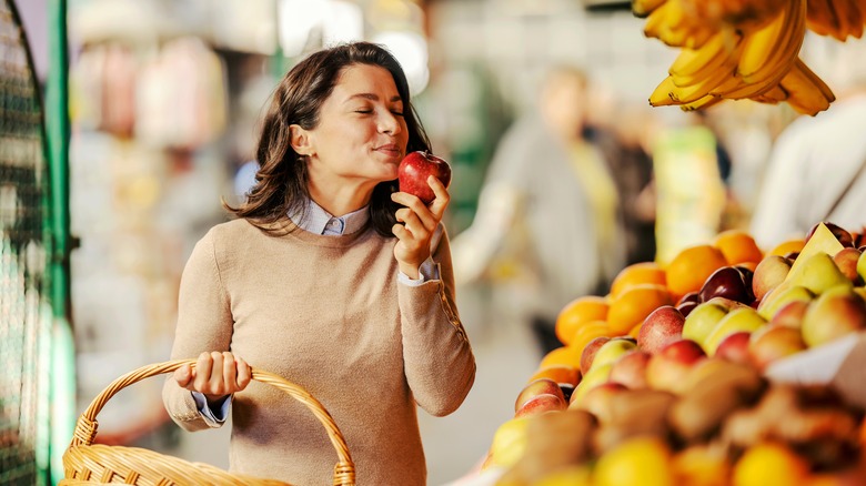 woman smelling apple in supermarket