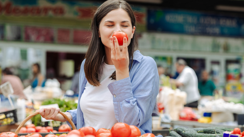 woman smelling tomato in supermarket