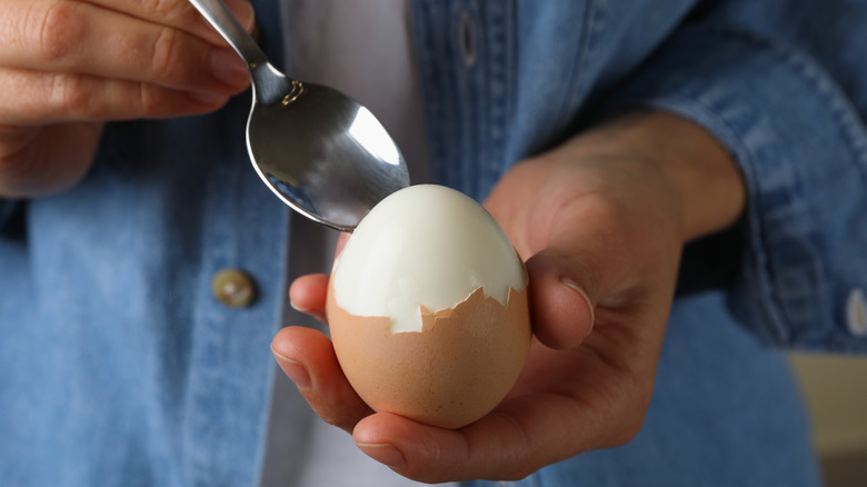 person peeling hard-boiled egg with spoon