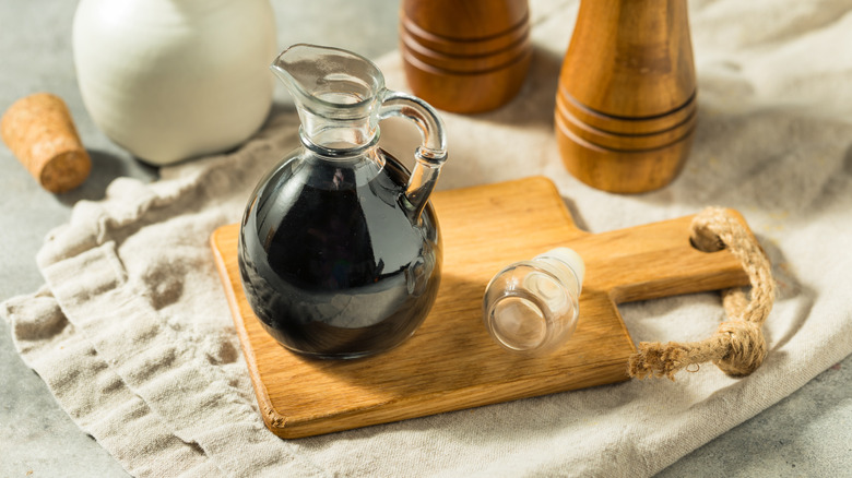 Balsamic glaze in glass jug on wooden cutting board