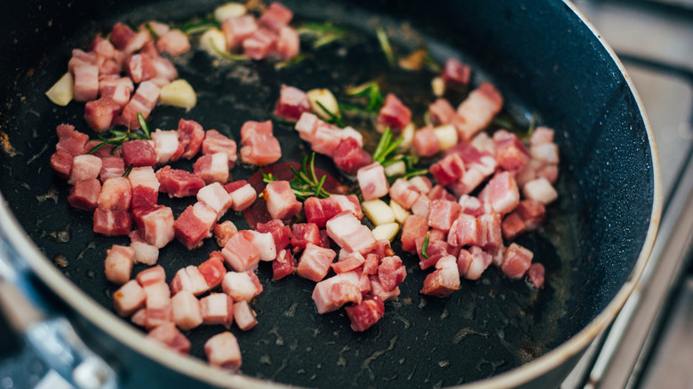 Cubed pancetta being fried in pan with rosemary