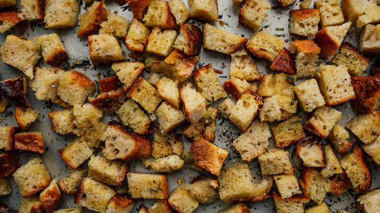 Oiled and herbed cubes of bread on baking sheet