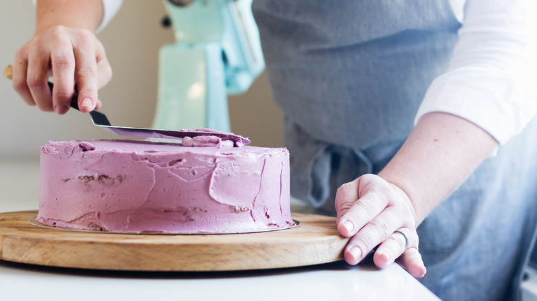 putting lilac frosting on cake