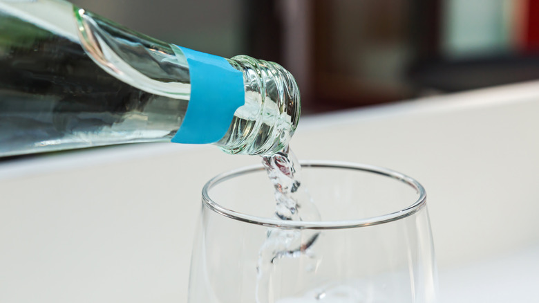 Sparkling water being poured from glass bottle into glass