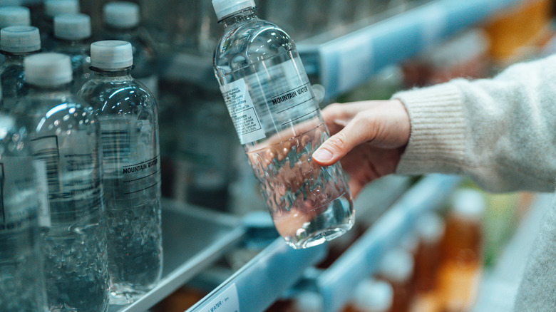 Person holding bottle of drinking water, which they've taken off a supermarket shelf