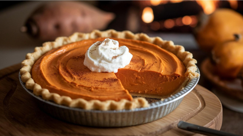 Whole sweet potato pie with slice missing topped with whipped cream