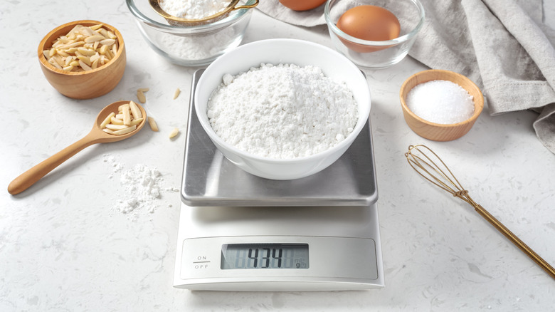 Digital scale with bowl of flour on it surrounded by other baking ingredients