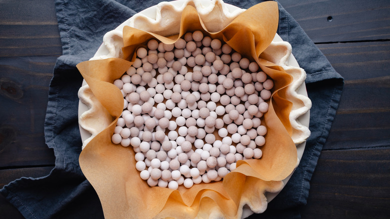 Top view of pie crust being prepared with pie weights for blind baking