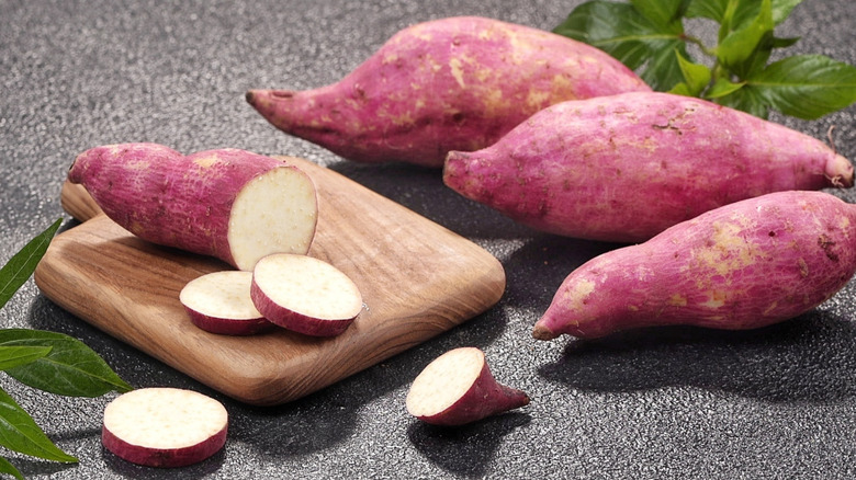 Whole sweet potatoes and sweet potato slices on wooden cutting board