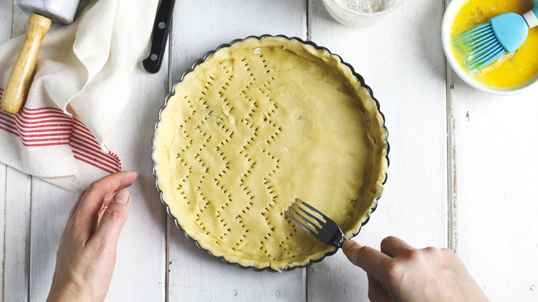 Hands docking homemade pie crust in a pan with a fork