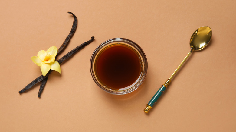 Bowl of vanilla extract with vanilla beans and metal spoon