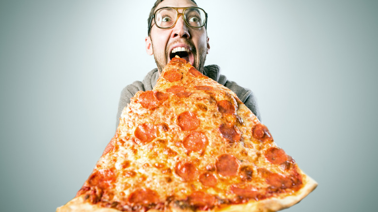 Excited adult man prepares to take a bite out of a massive slice of pizza