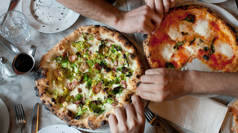 Hands dig into two pizzas on restaurant table