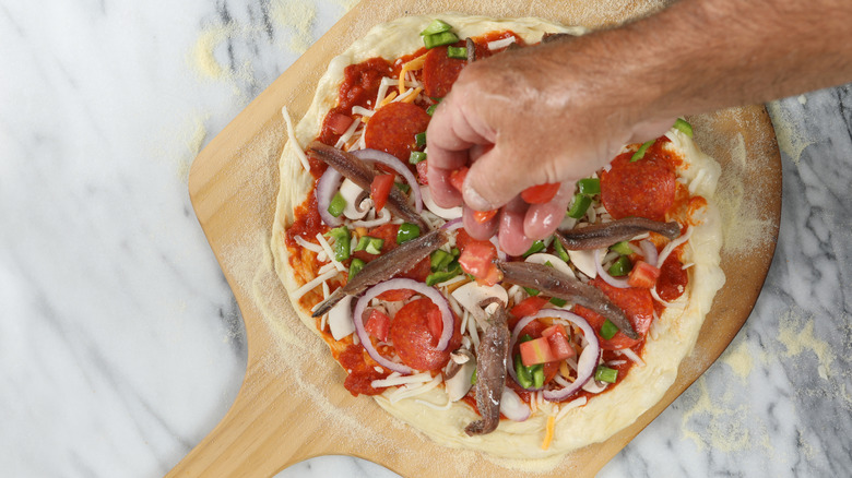 Person putting toppings onto a pizza, which already had anchovies, green chilies, and pepperoni slices