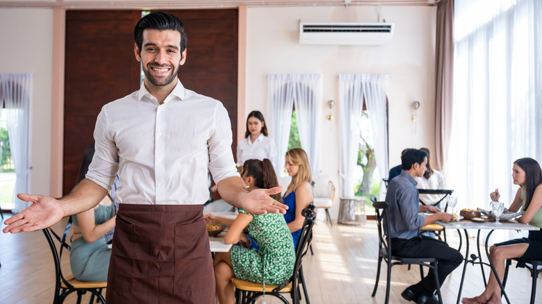 Male server standing in restaurant, smiling, with his hands outstretched