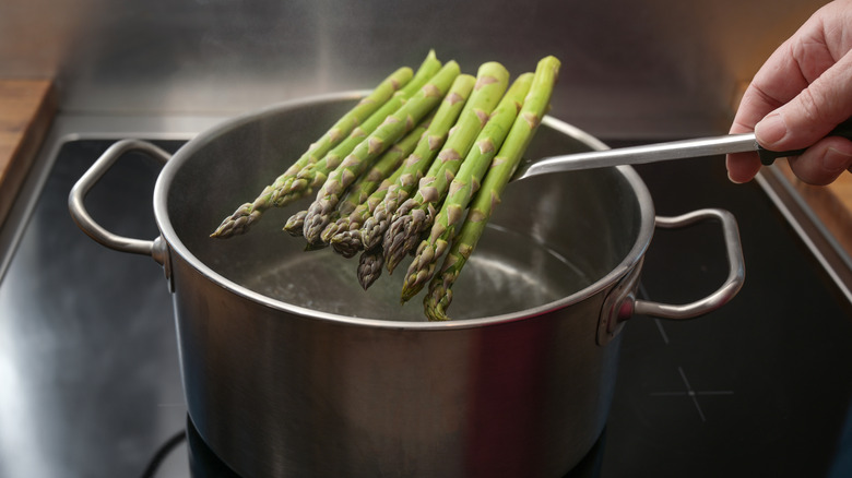 person holding asparagus above boiling pot