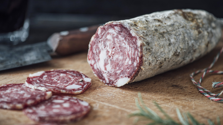 Salami on wooden board, with pieces sliced from it