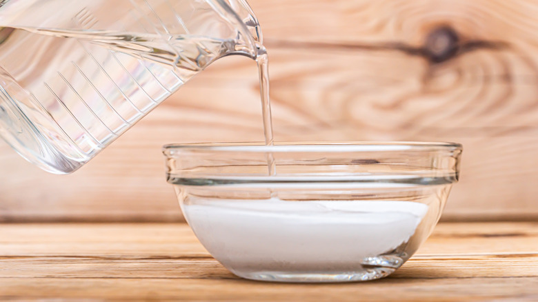 water pouring into clear bowl baking powder wood background