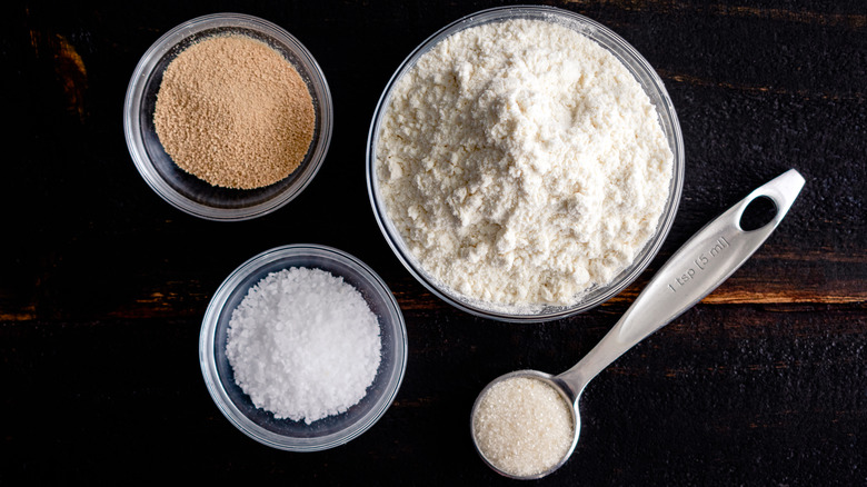 salt, flour, sugar, and yeast clear bowls dark wood table