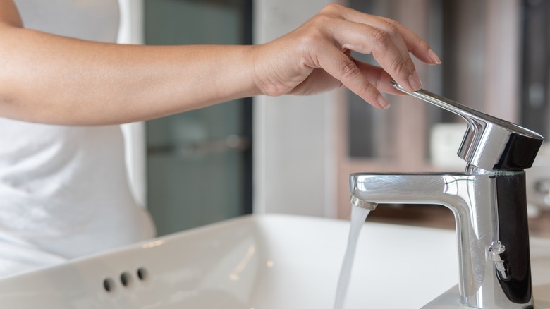 hand turning on steel faucet white sink