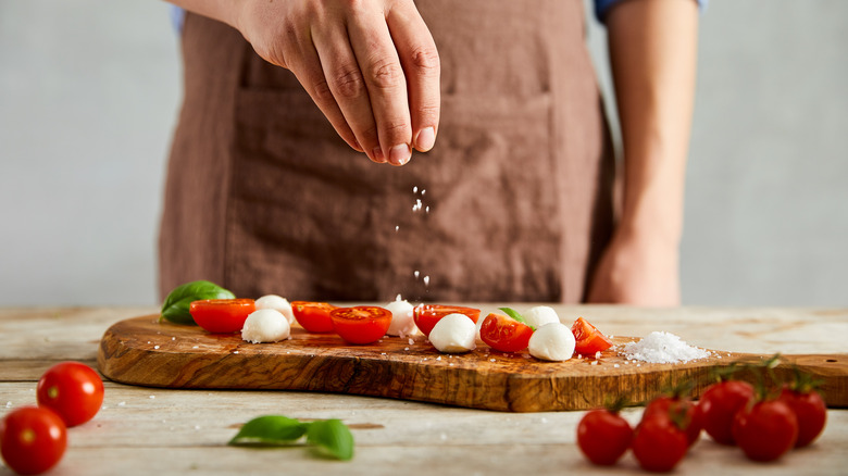 person salting veggies and cheese