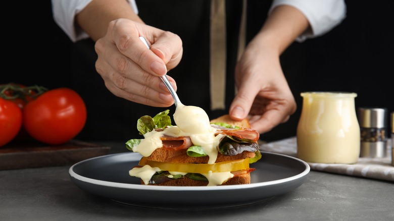 person spooning mayo on sandwich