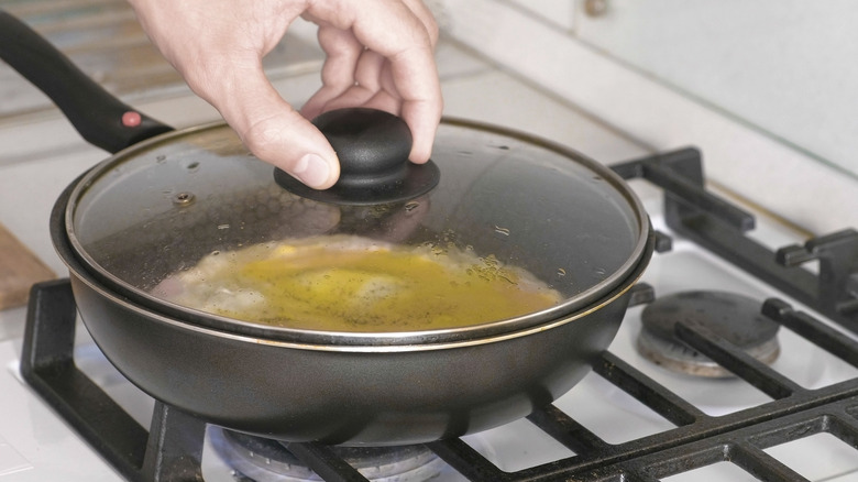 person placing lid on frying pan