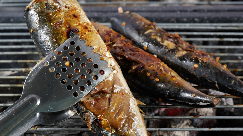 Metallic tongs flipping fish on grill