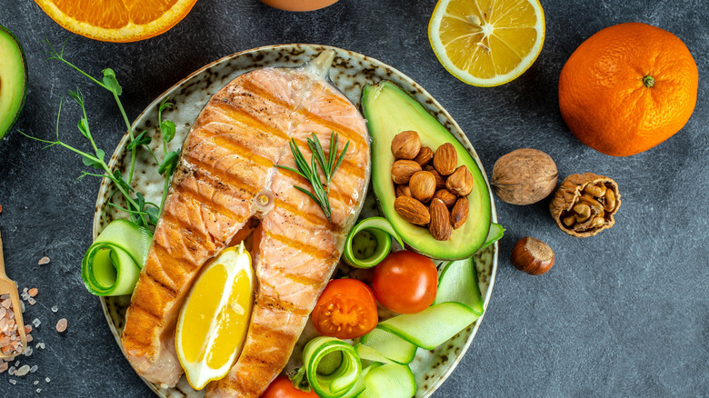 Grilled salmon steak on plate, surrounded by healthy keto foods